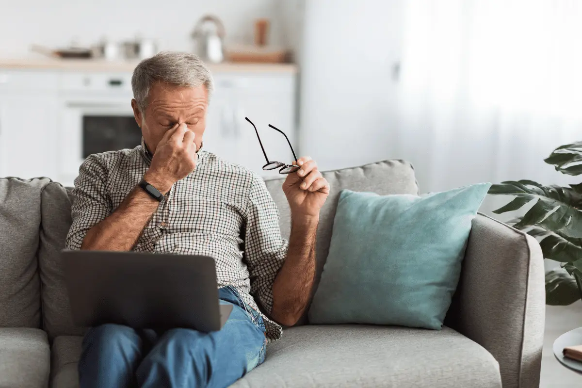 an older man taking off his glasses after working on a laptop