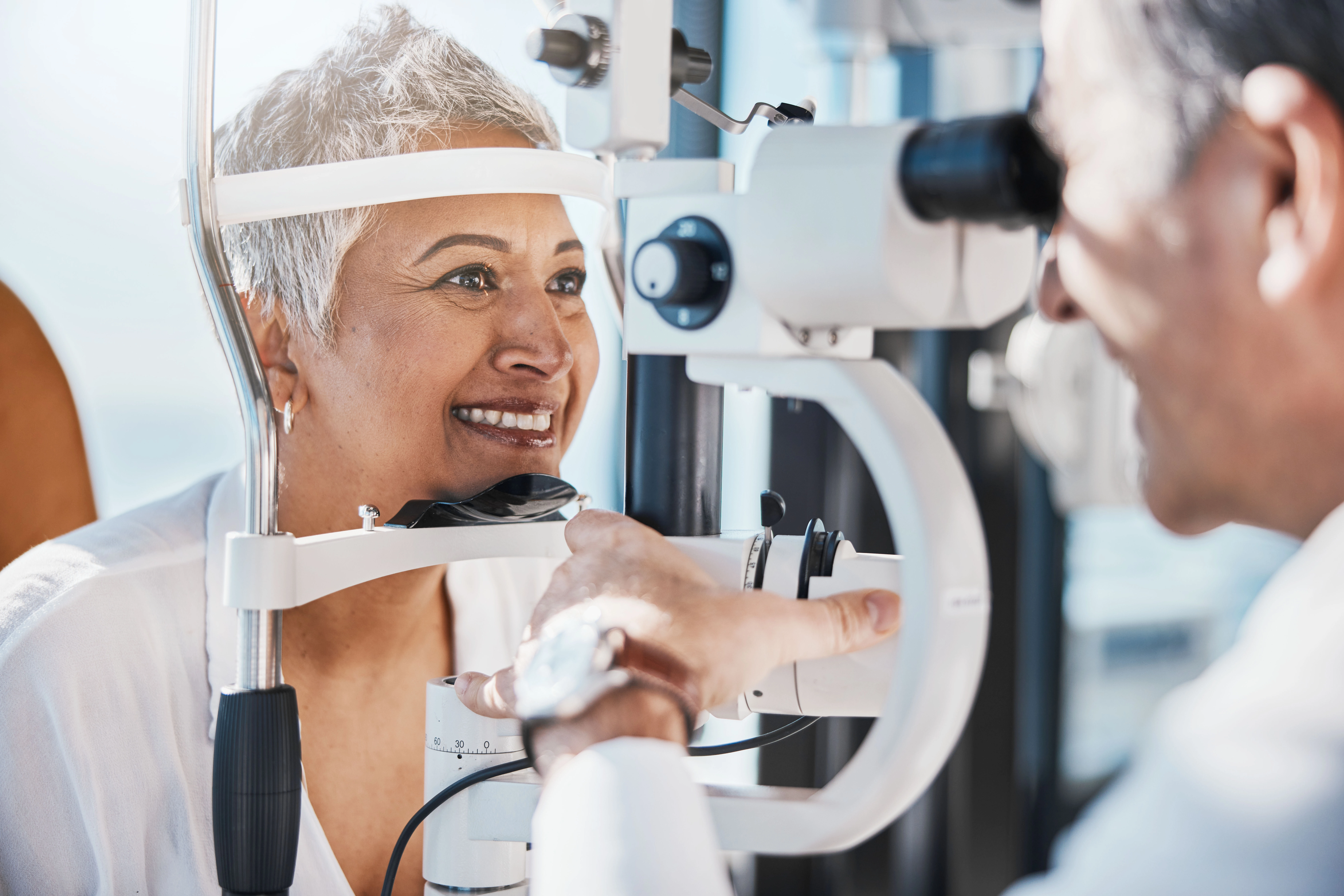 A smiling older woman getting her eyes examined by her doctor.