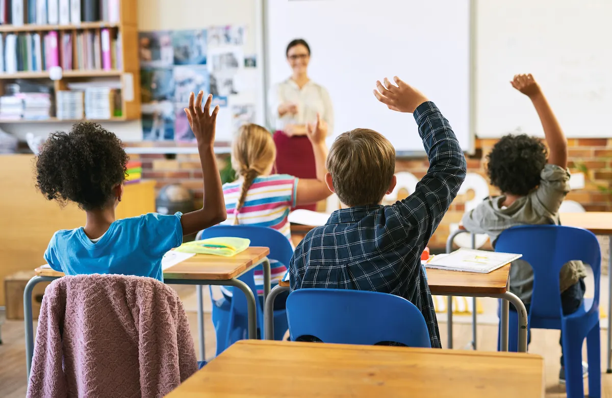 children raising hands in classroom